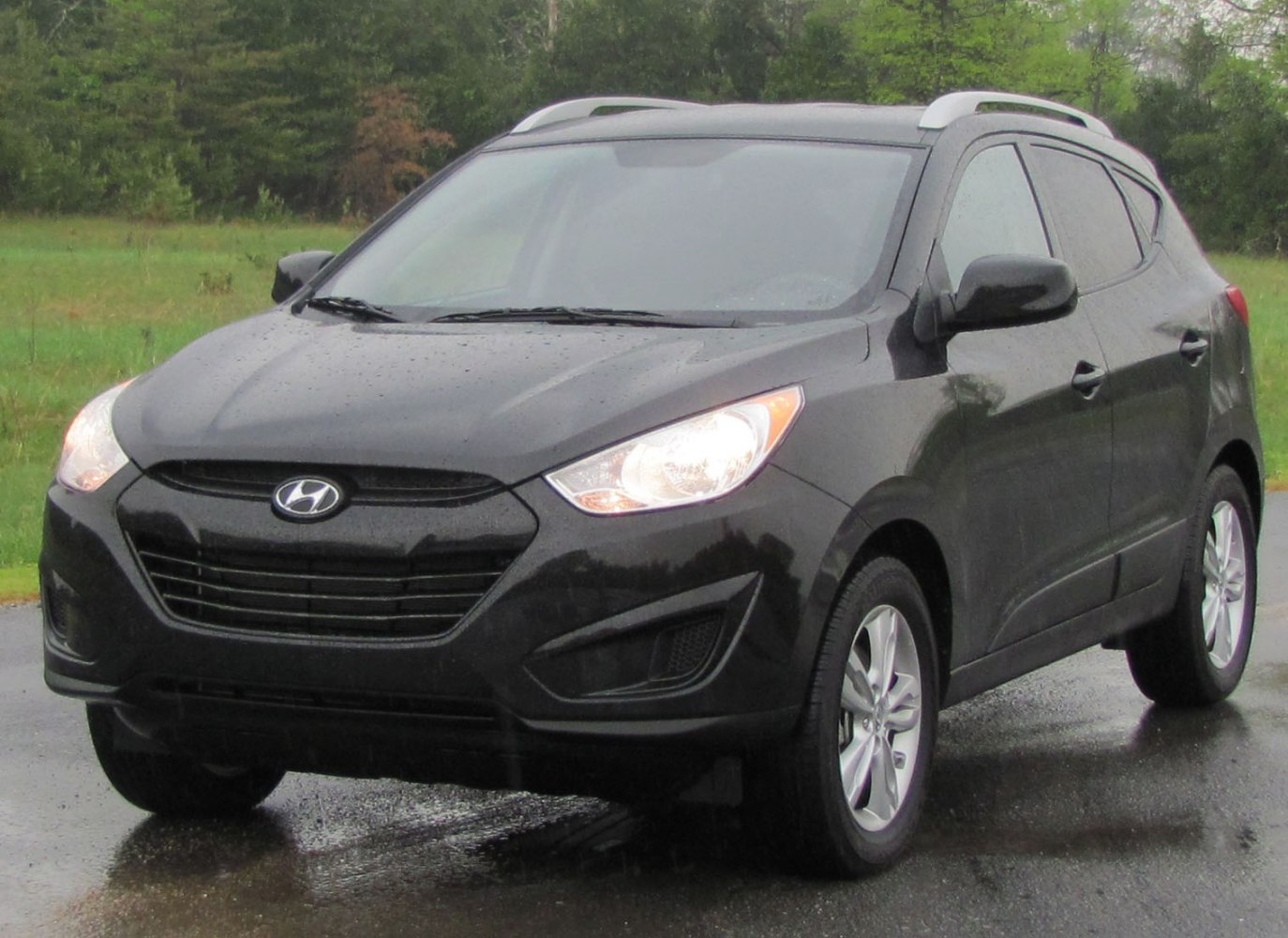 Front view of a black compact SUV with headlights on, on a wet road.