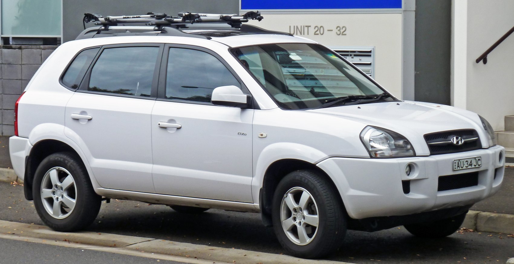 White compact SUV with roof racks, side view.