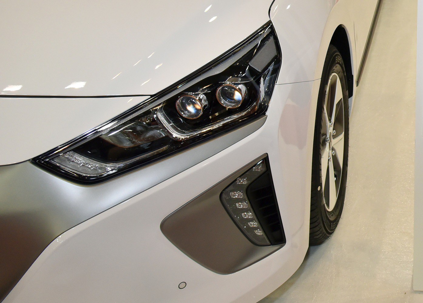 Modern front headlight and aerodynamic wheel design on a white vehicle.