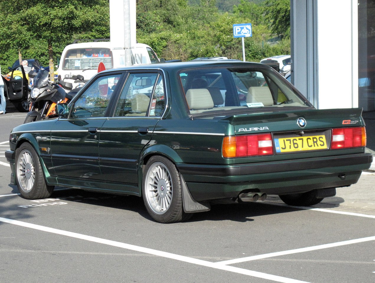 Rear view of dark green sedan with multi-spoke wheels and rear spoiler
