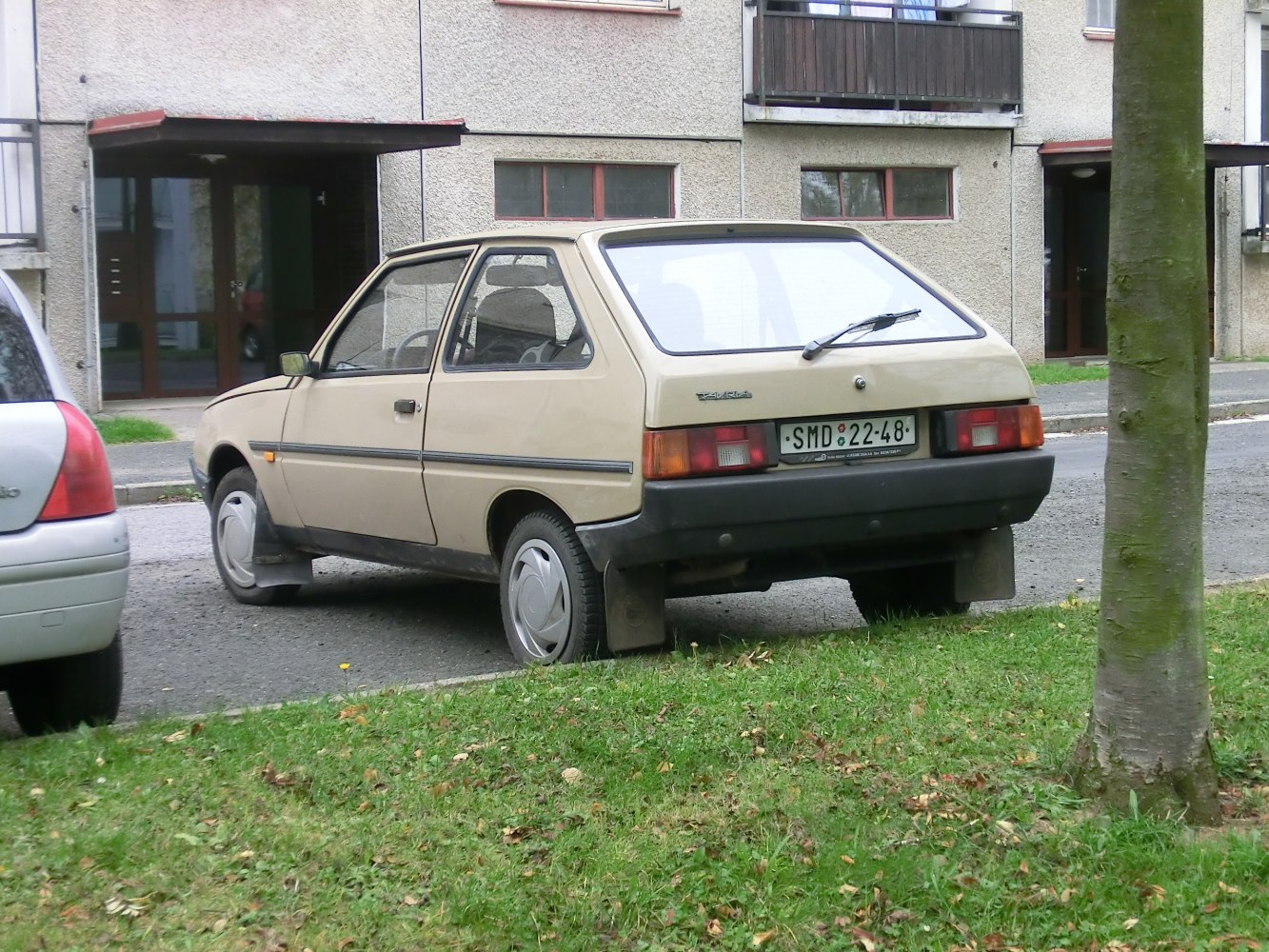 Rear three-quarter view of a beige 3-door hatchback with black bumper and rear windshield wiper