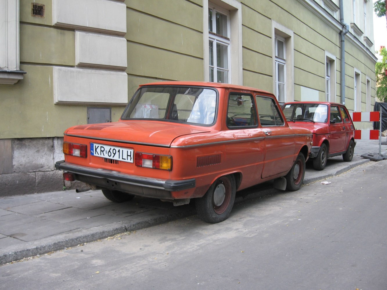 Orange vintage compact four-door sedan rear view with classic tail lights and bumper.