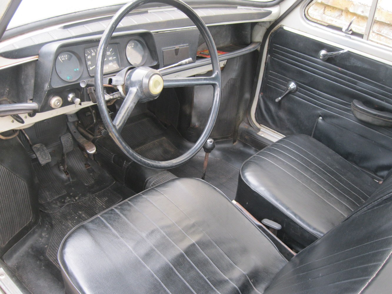 Vintage car interior with black seats, large steering wheel, and manual gear shift