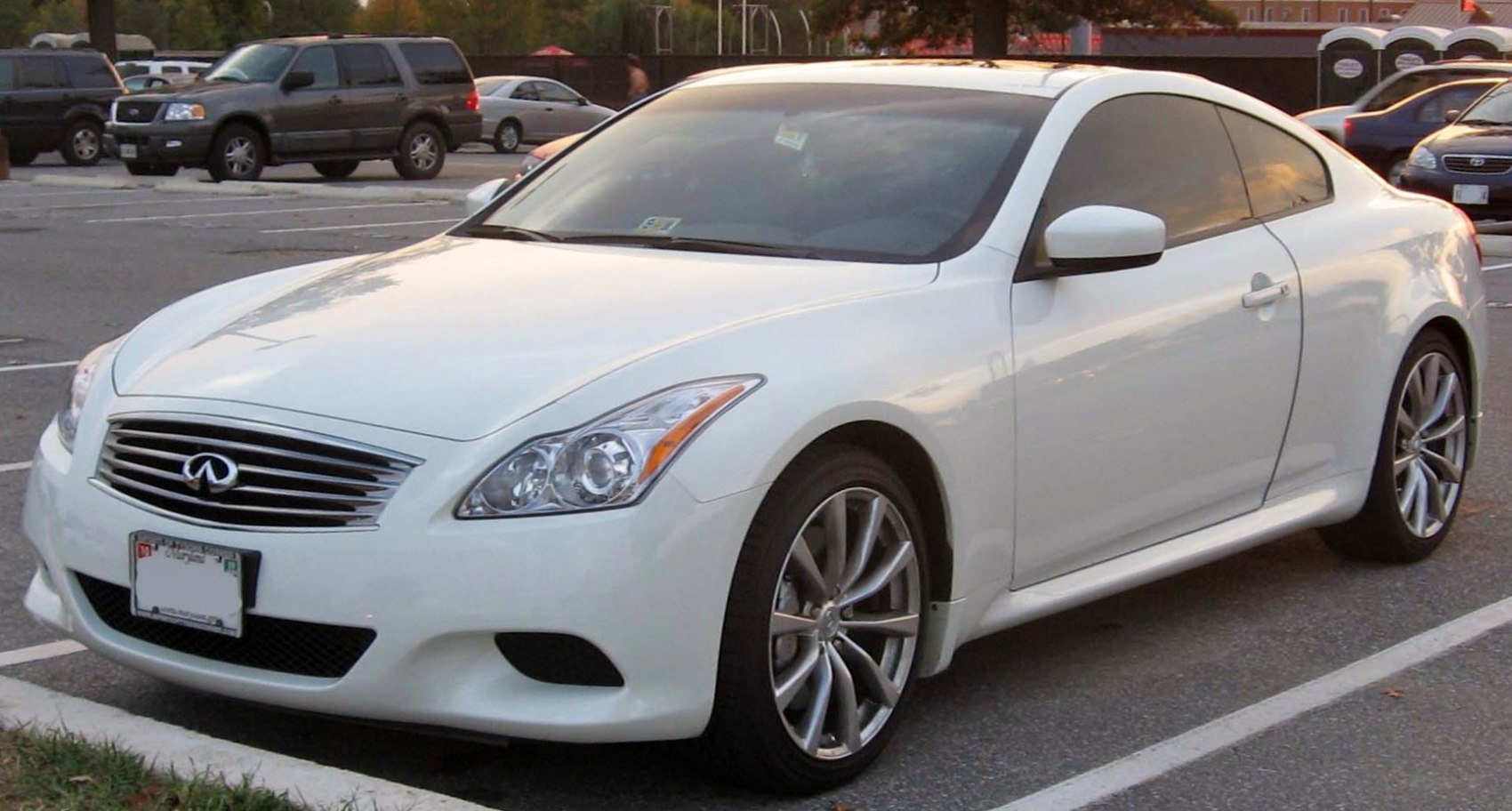 White coupe with front grille, headlights, and alloy wheels in parking lot