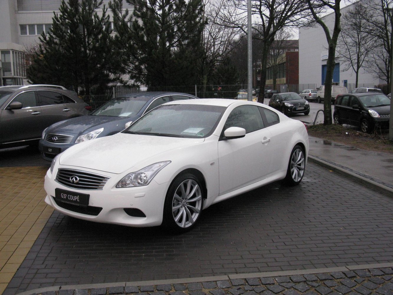 Sporty white 2-door coupe with large alloy wheels on wet pavement.