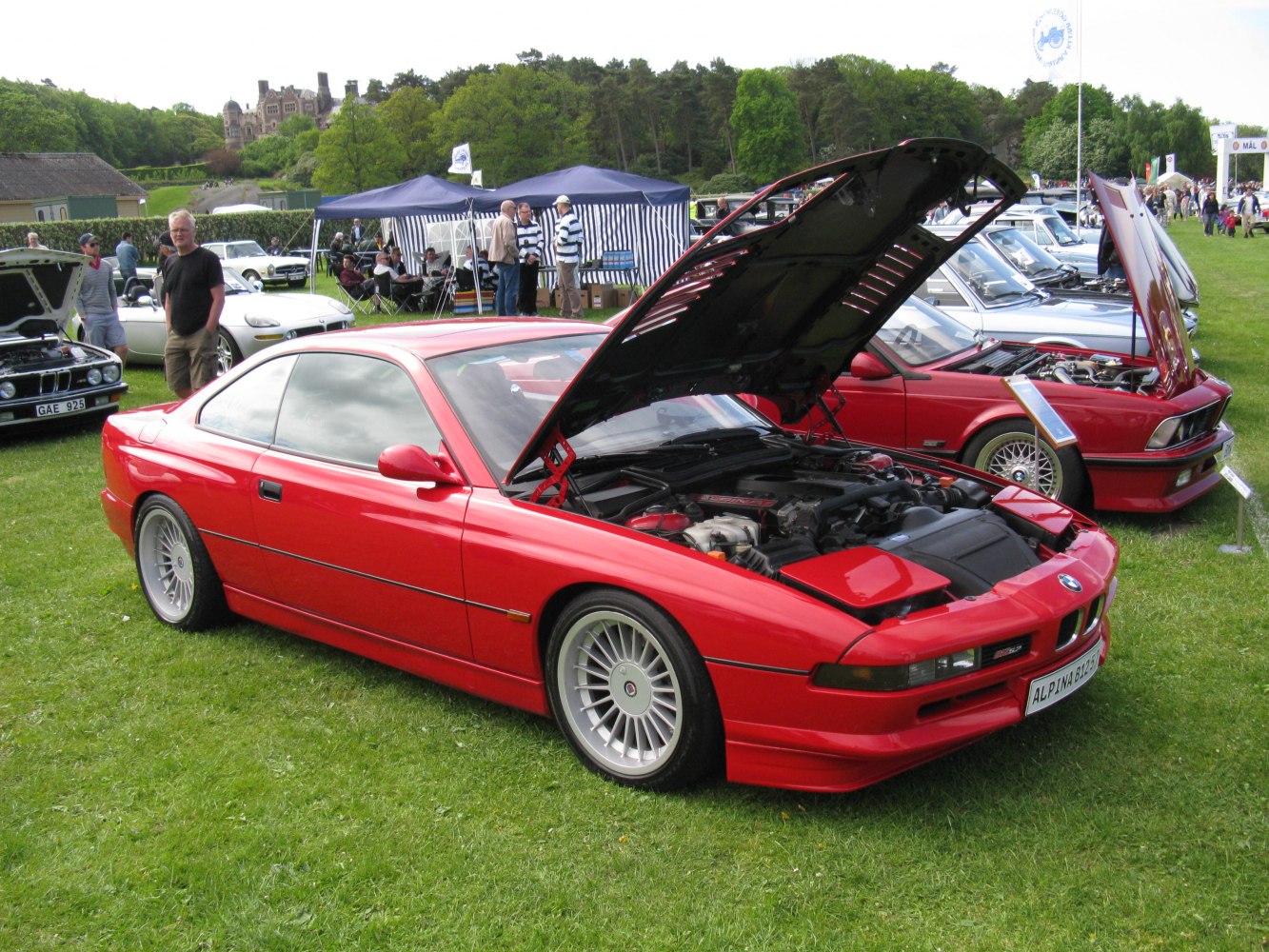 Red classic coupe with open hood and visible engine components at outdoor car show