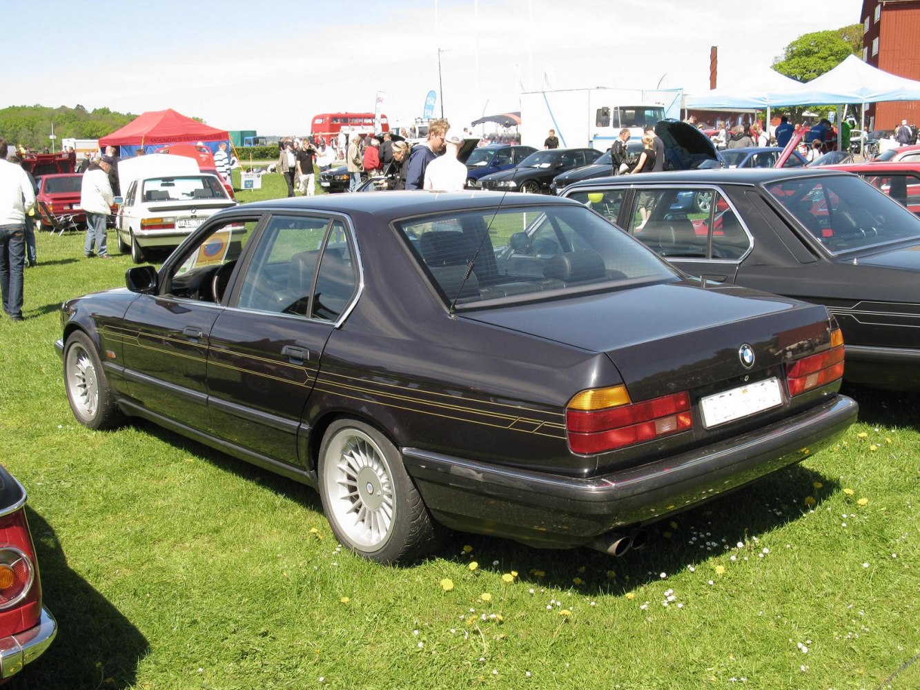 Rear side view of a luxury sedan with distinctive multi-spoke alloy wheels and stripe detailing.