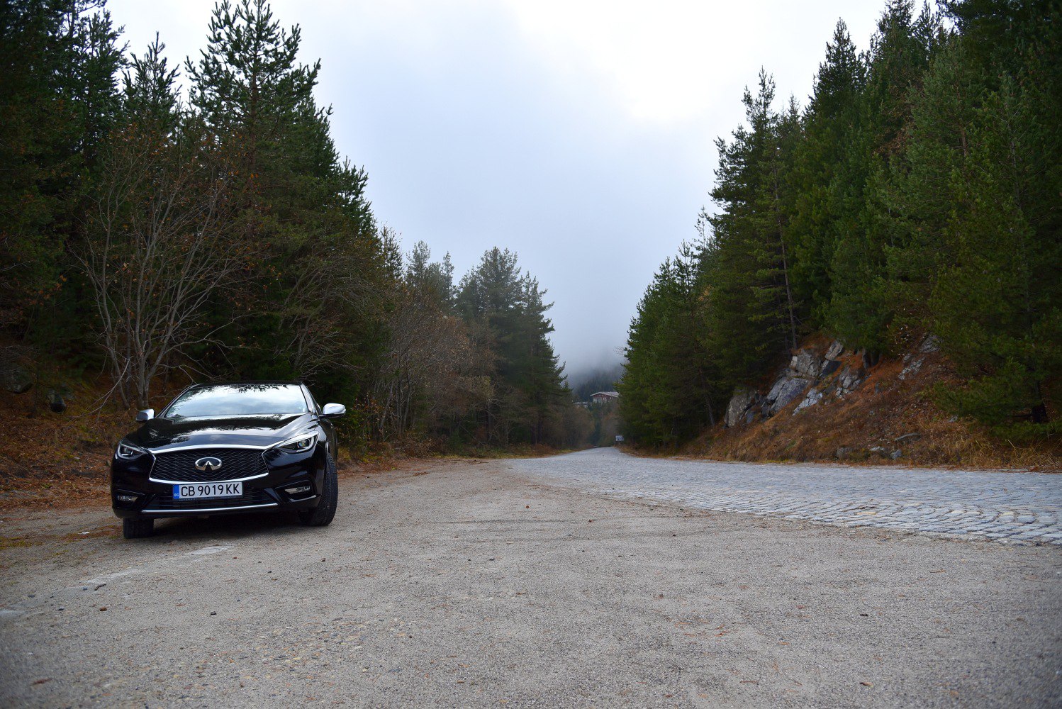 Front view of sleek black vehicle with distinctive grille on gravel road.