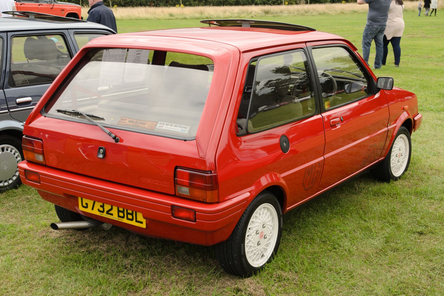 Red hatchback with sunroof and white mesh alloy wheels on grass