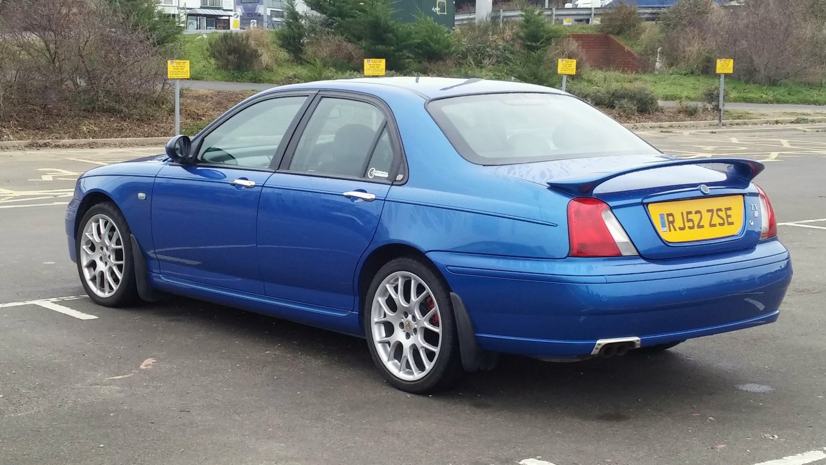 Blue sedan with rear spoiler, alloy wheels, and dual exhausts