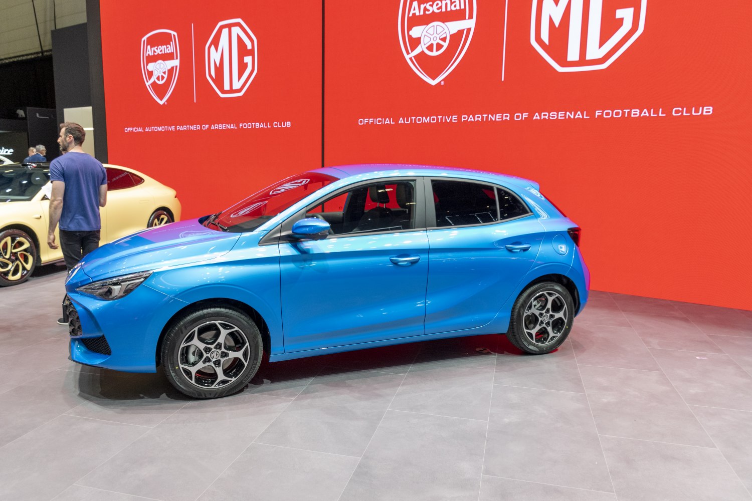 Side profile of a blue compact hatchback with sporty alloy wheels.