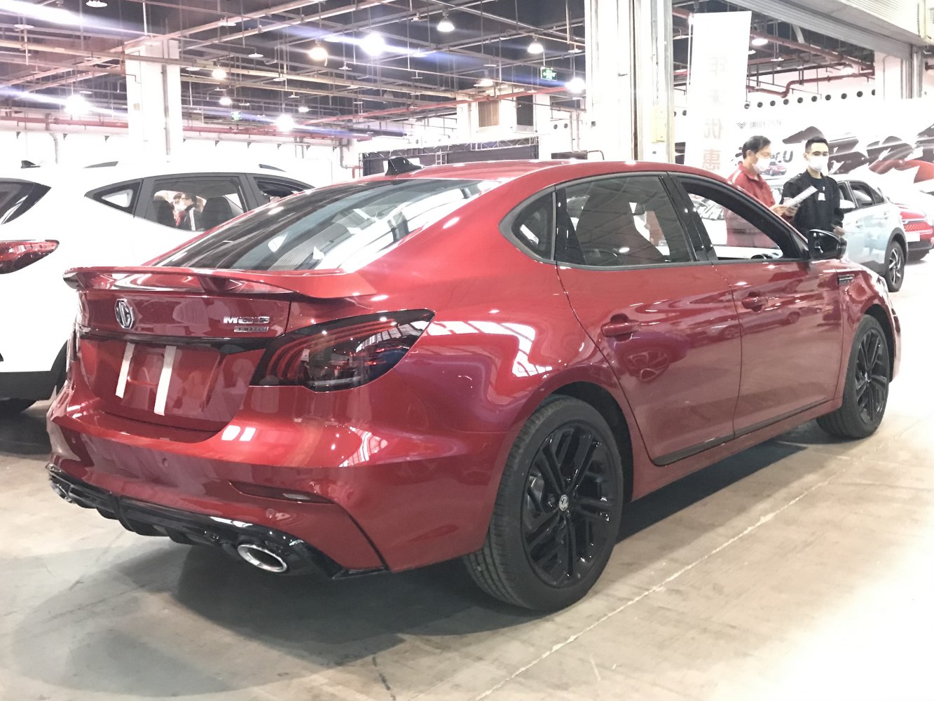 Red sedan rear side with black wheels, spoiler, and dual exhaust