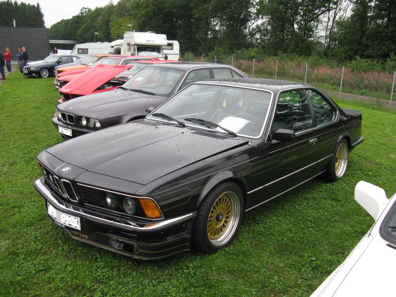 Front angled view of black vintage coupe with gold wheels and rain droplets