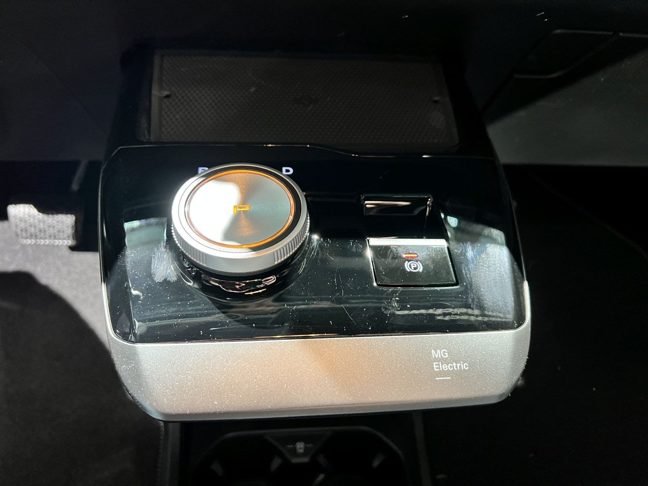 Rotary gear selector dial and electric parking brake switch on a glossy console surface