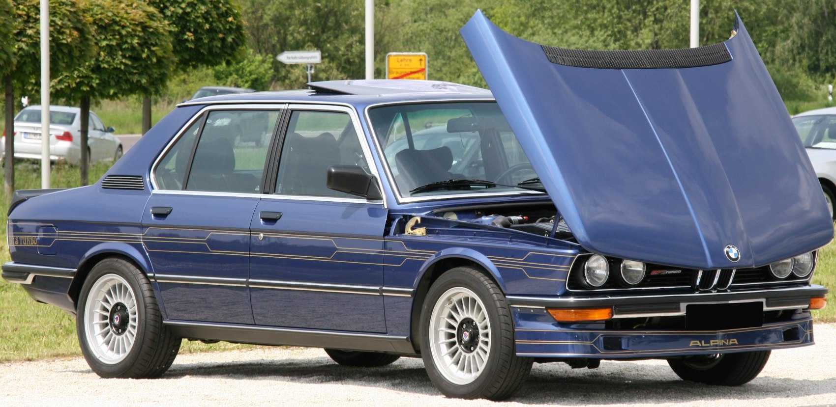 Blue sedan with open hood and multi-spoke alloy wheels