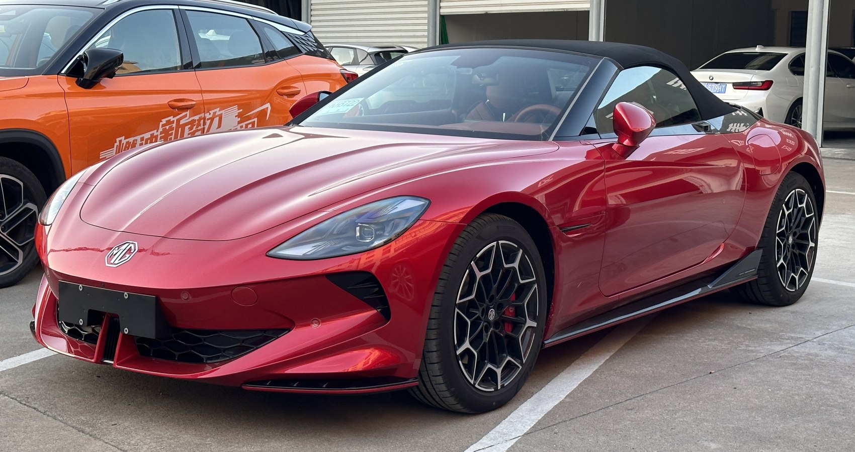 Red convertible sports car with black soft top and honeycomb pattern wheels