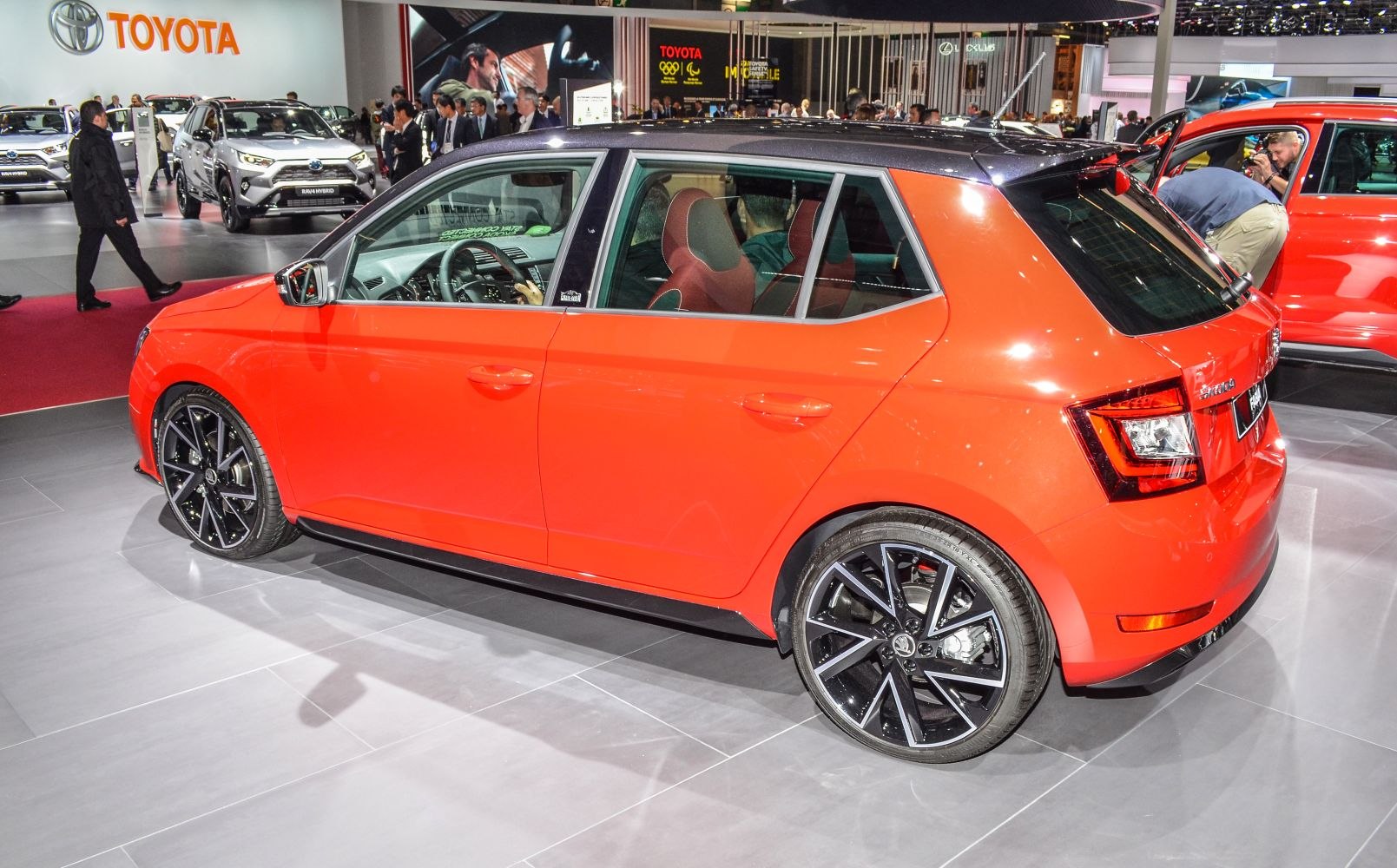 Red hatchback side view with black alloy wheels and sporty design.