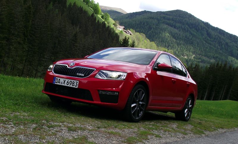Red sedan on grass with forest and mountains backdrop