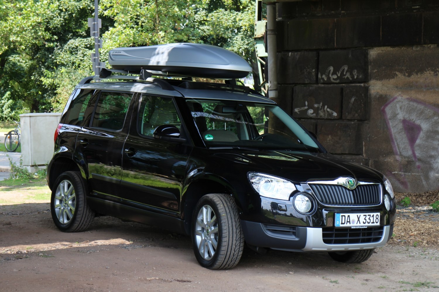 Black SUV with rooftop cargo box under a bridge.