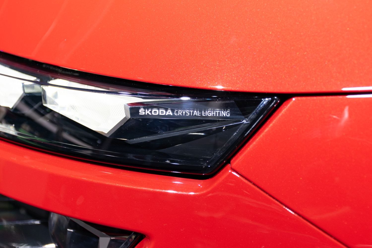 Close-up of a modern headlight with crystal lighting design on red car body.