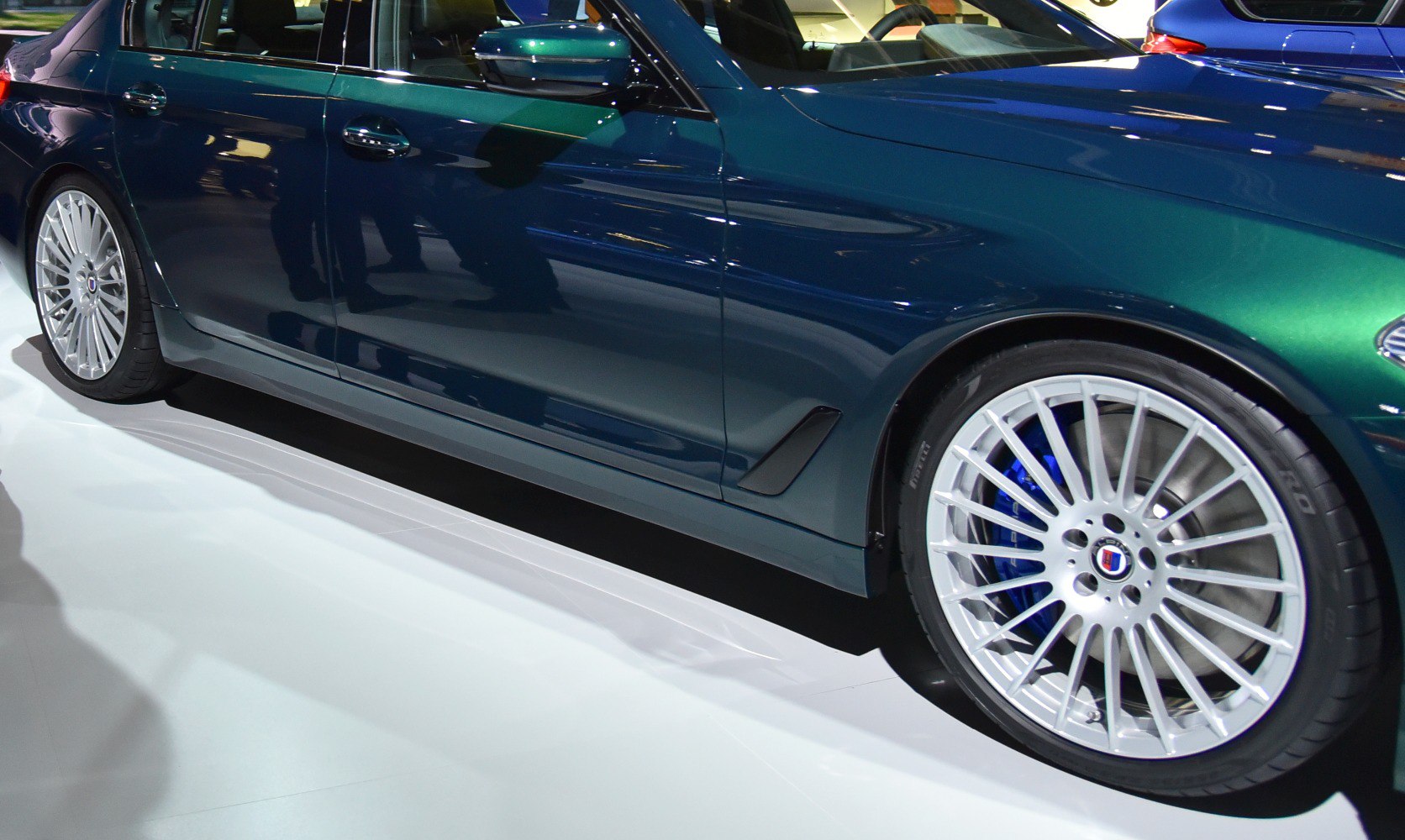 Side profile showing sleek door and multi-spoke alloy wheel with blue brake caliper