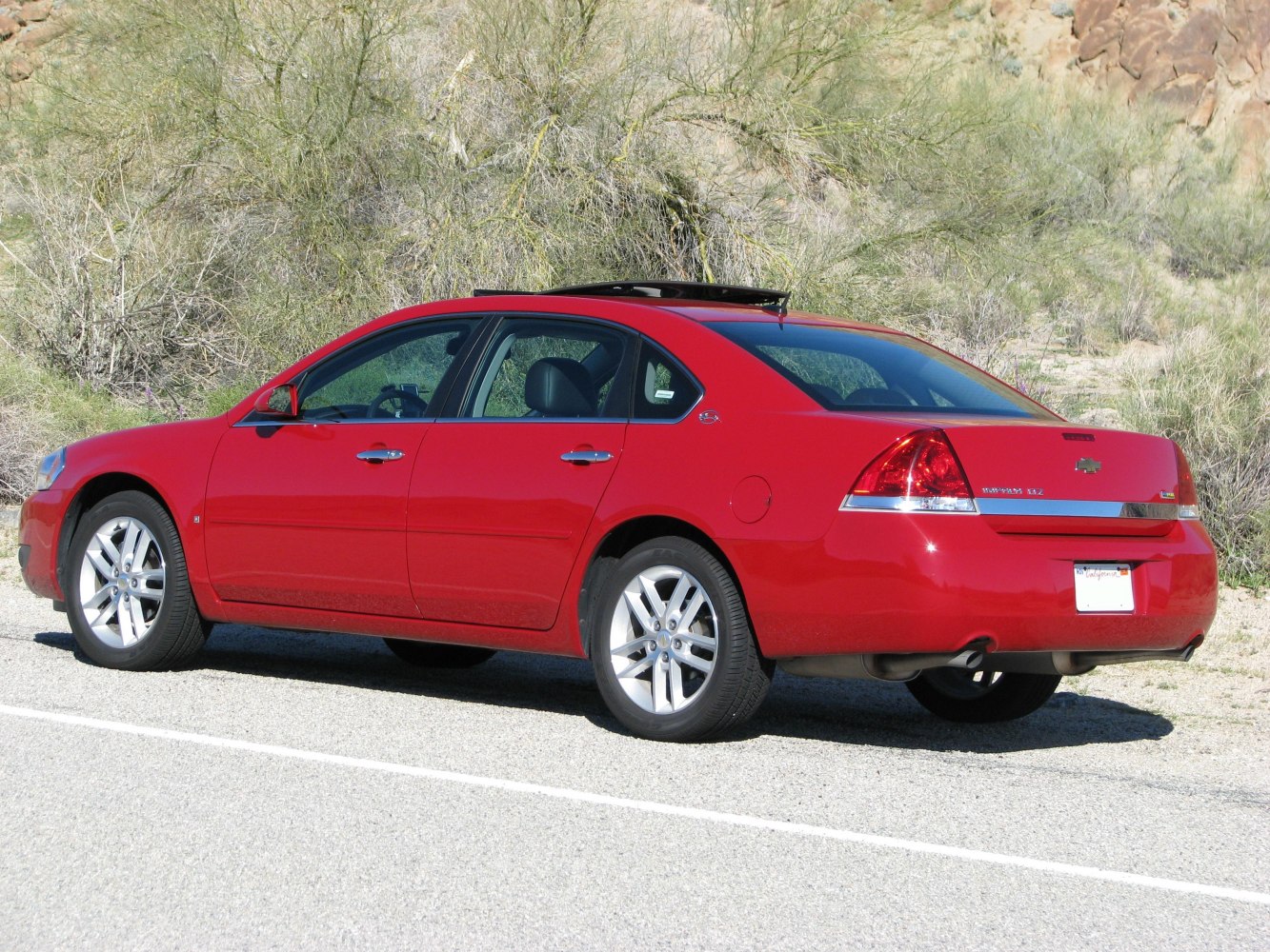 Red sedan with sunroof and alloy wheels parked on roadside