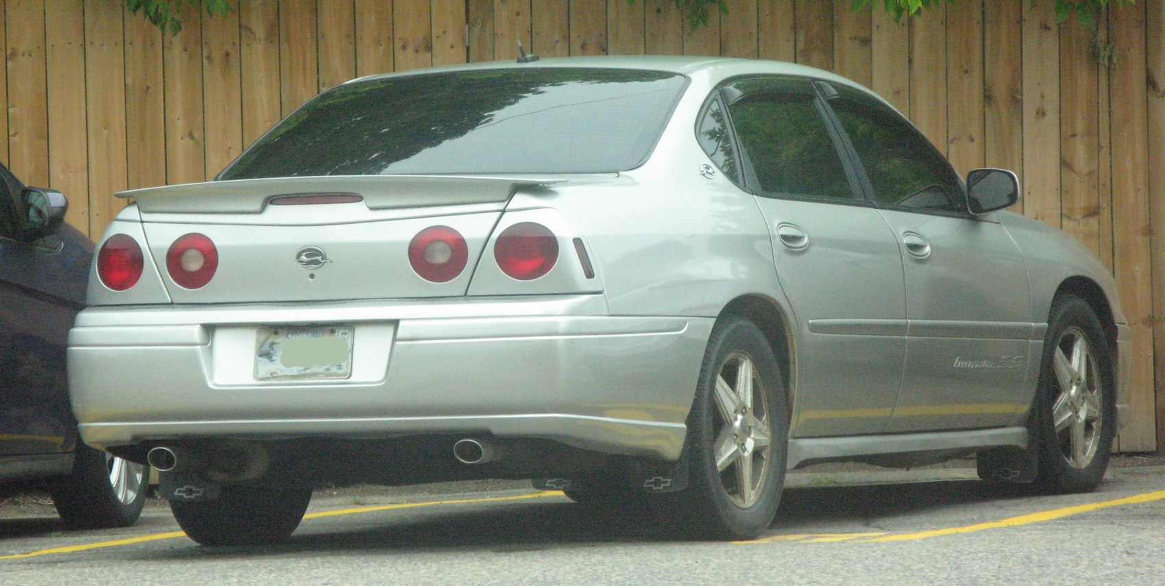 Rear of silver sedan with round taillights, spoiler, and dual exhaust
