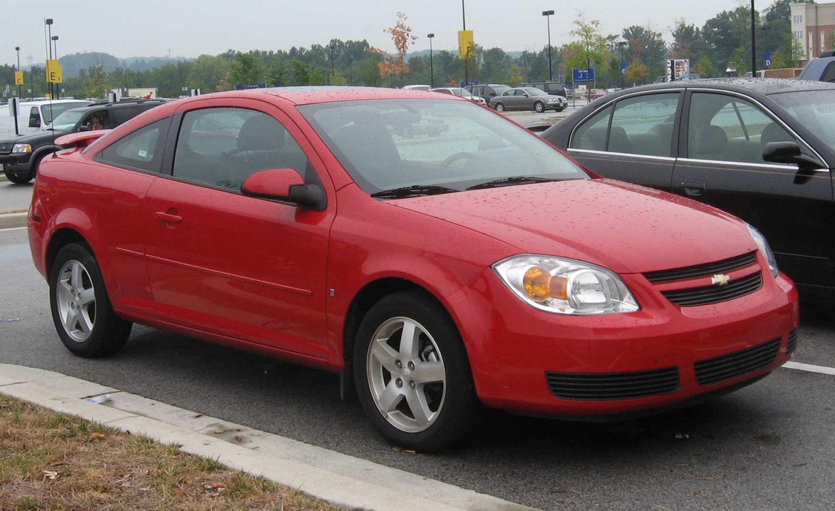 Red 2-door coupe car parked front-side view with alloy wheels.