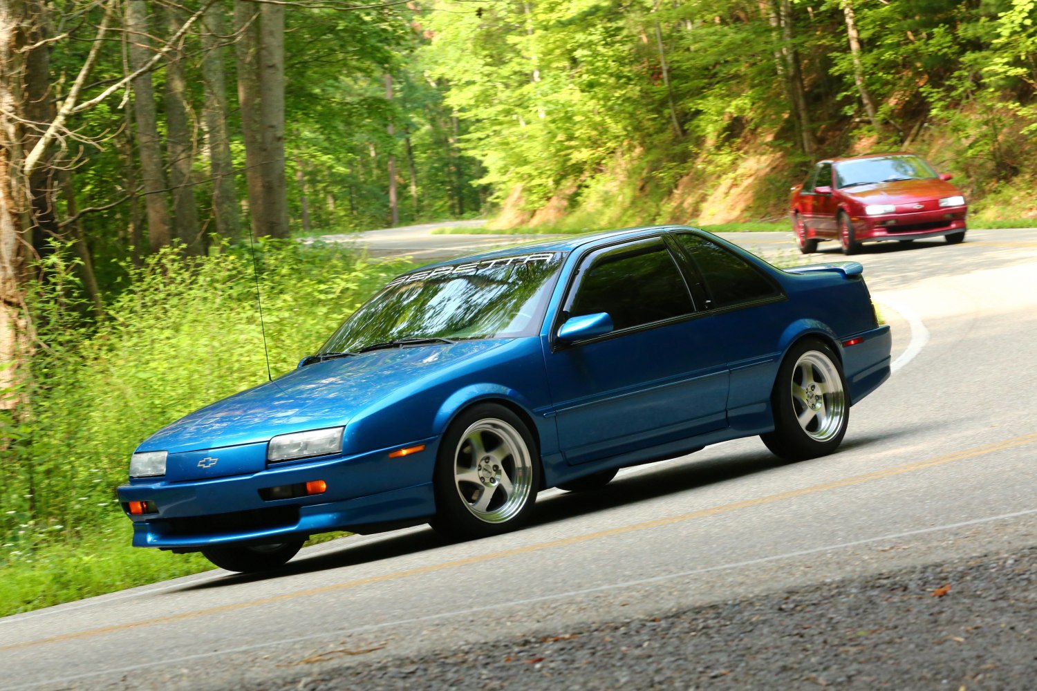 Classic wedge-shaped two-door coupe speeding on curvy forest road