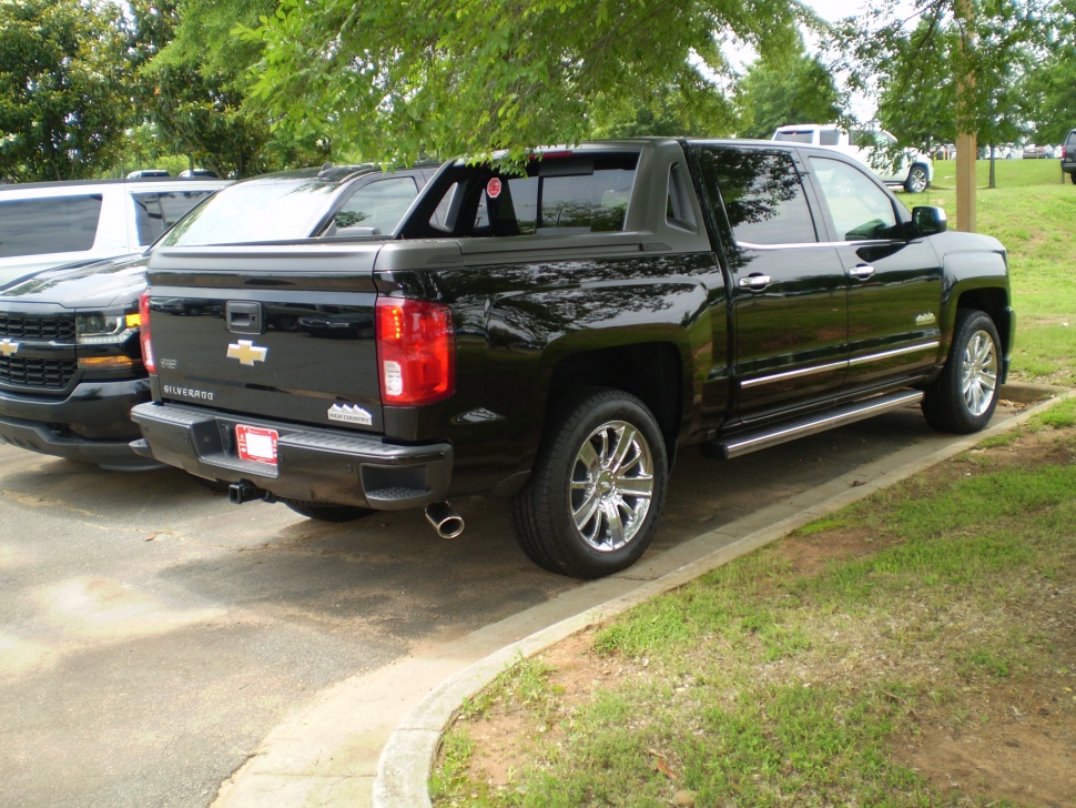Rear and side view of a black pickup with chrome wheels and covered bed