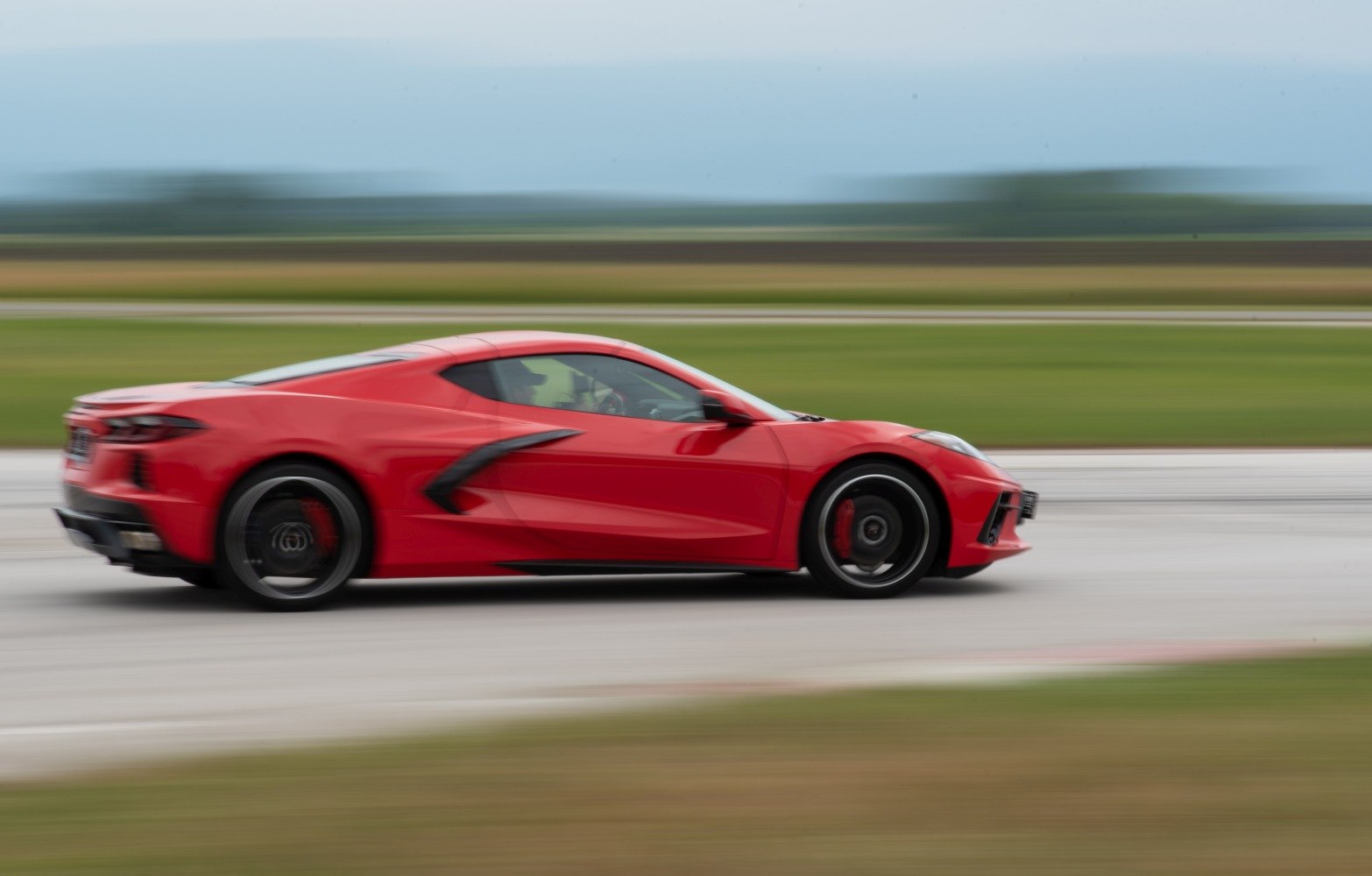 Red mid-engine coupe speeding with aerodynamic design and sharp side contours
