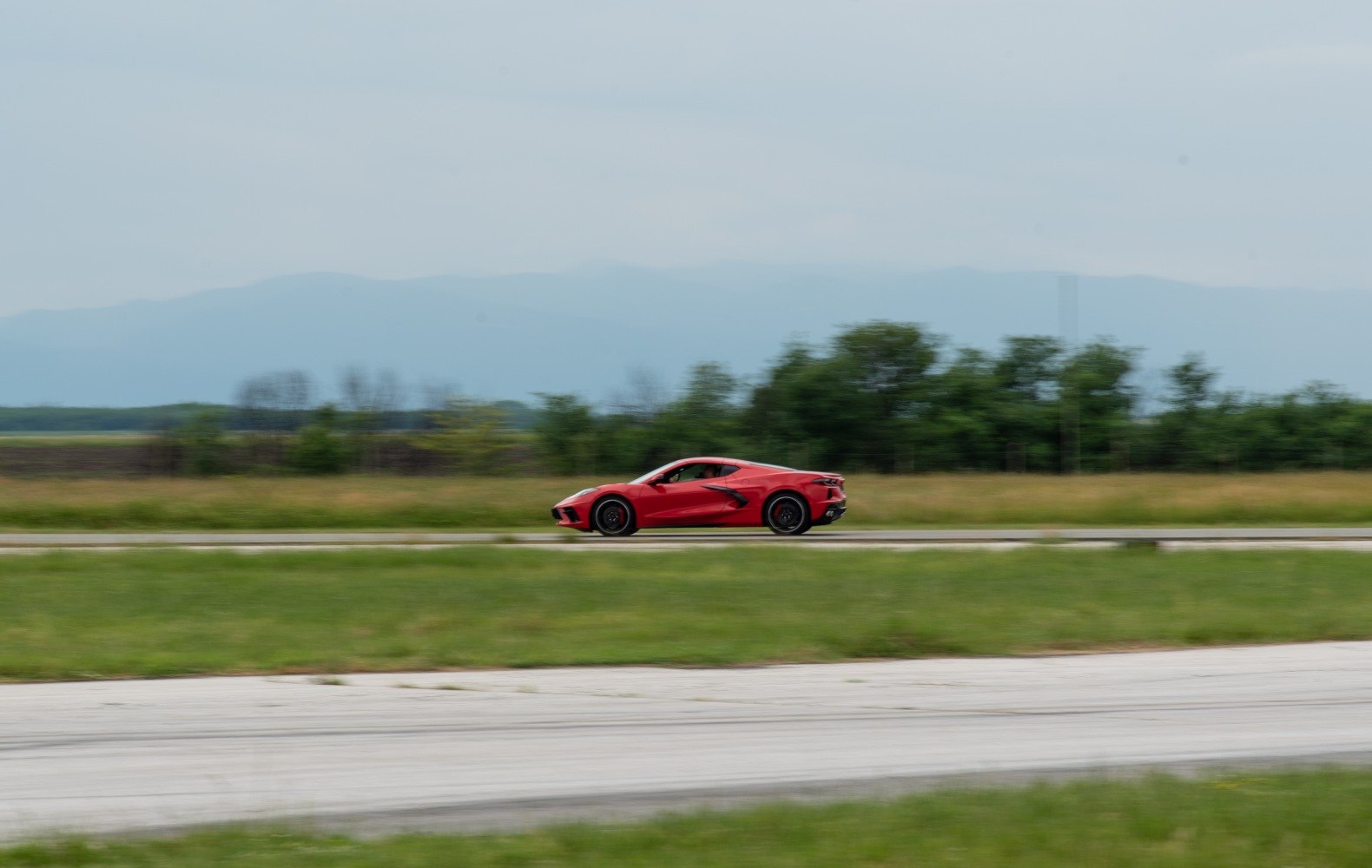Red mid-engine coupe speeding on runway, side profile
