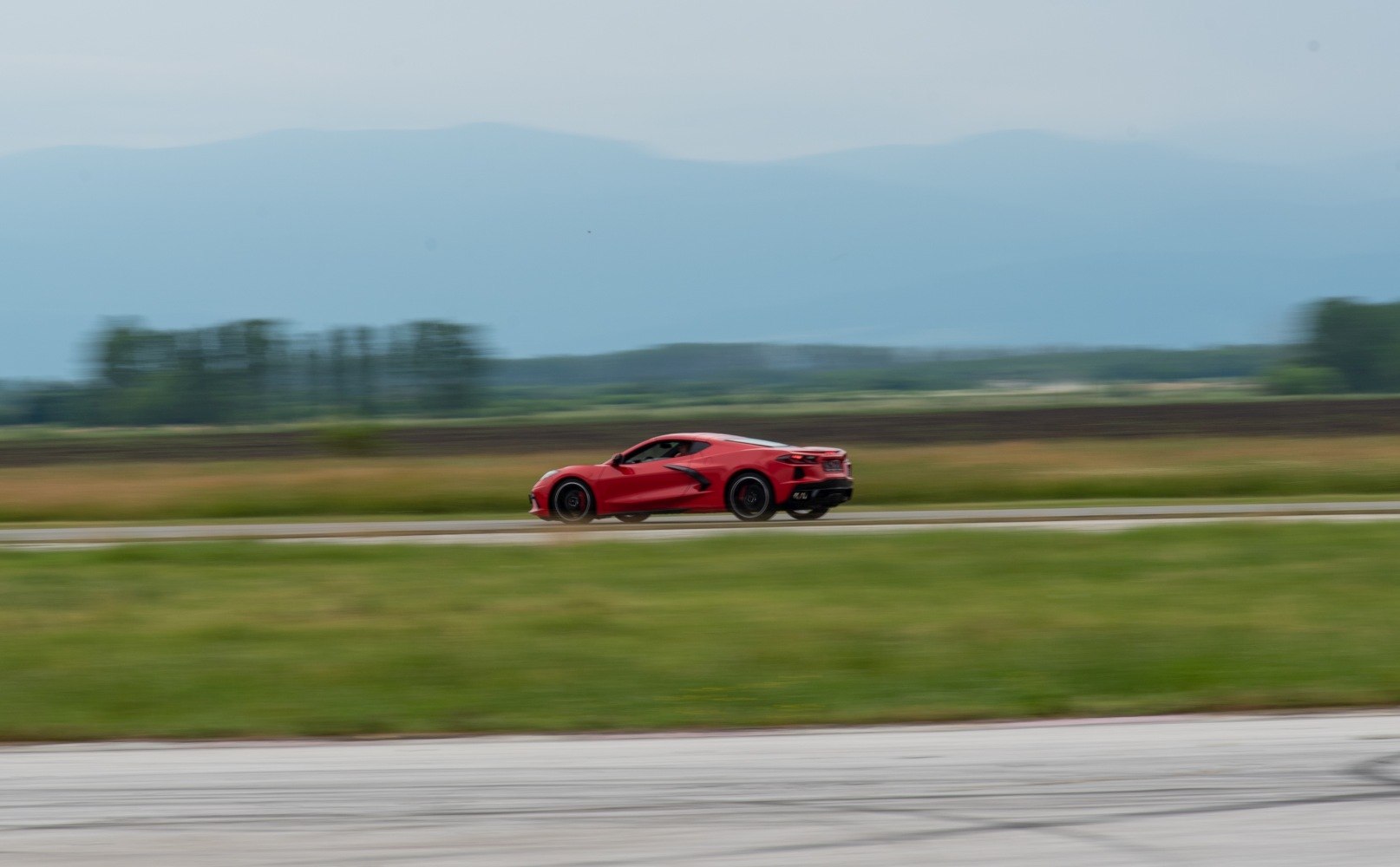Side view of a red sports coupe speeding on a road