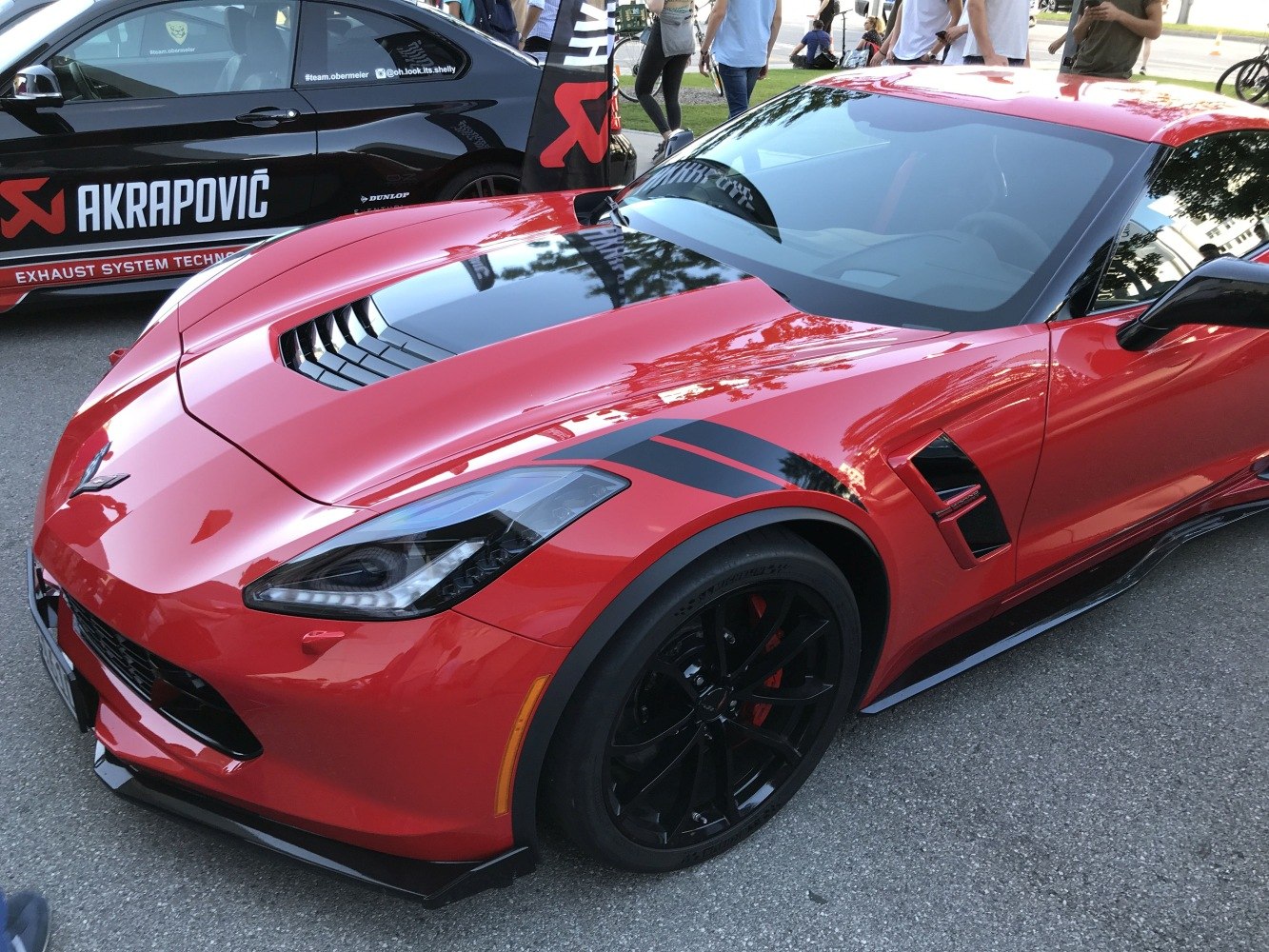 Close-up of a red sports car front hood with vent, black racing stripes, and black wheel.