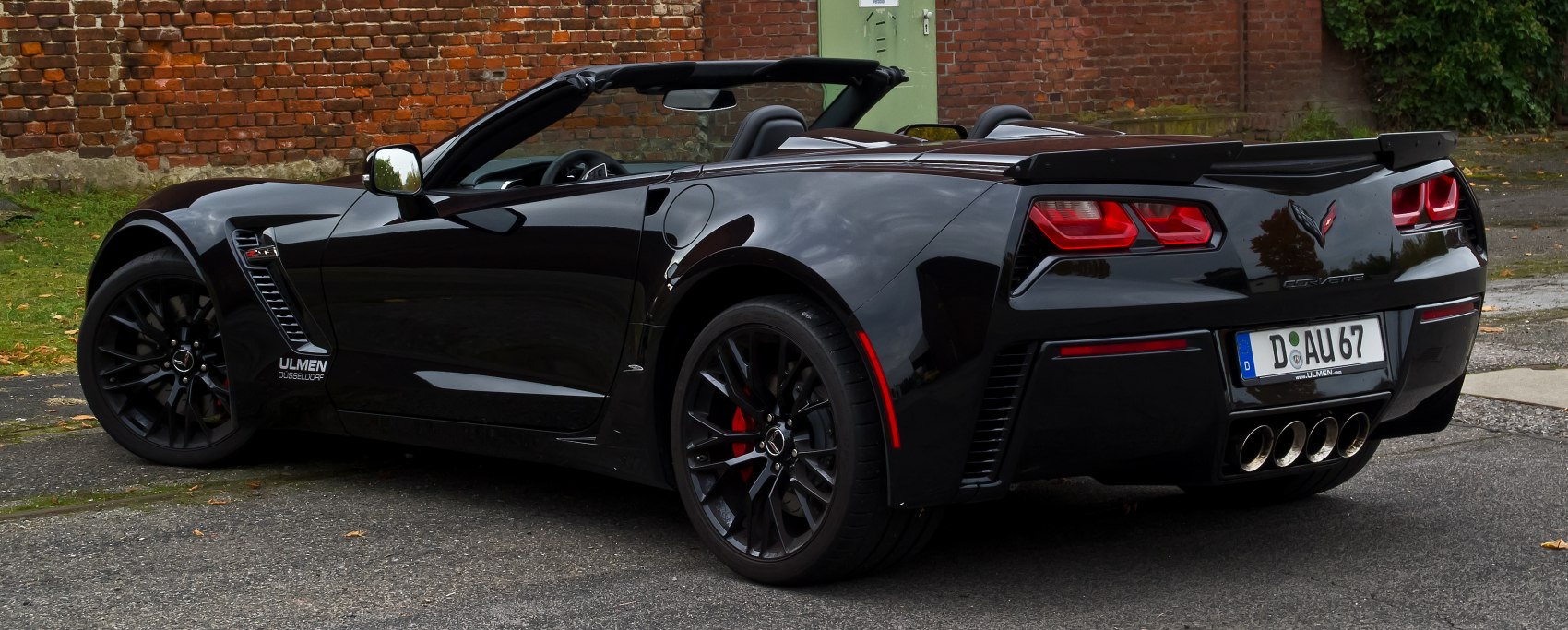 Rear side view of a convertible sports car with quad exhausts and black rims