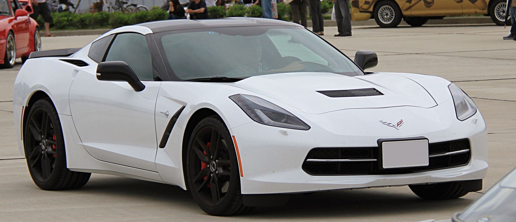 White coupe with angular headlights and black deep-dish rims, front-side view.