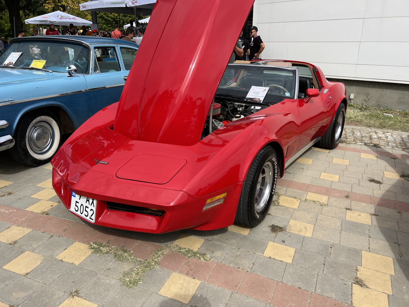 Red Corvette C3 coupe with raised hood showing engine and sleek body.