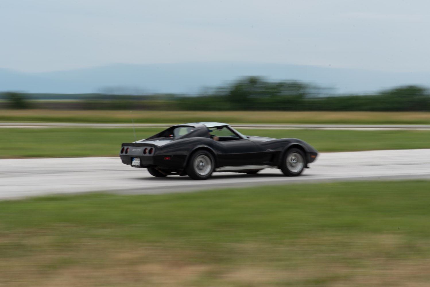 Rear side view of a classic sports coupe in motion on a track