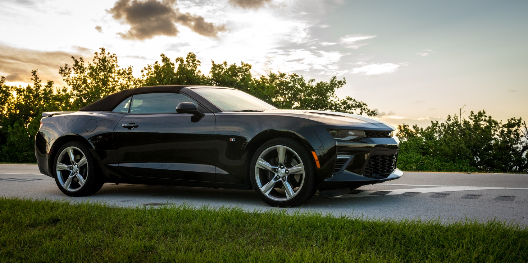 Front-side view of a sleek black convertible with alloy wheels at sunset