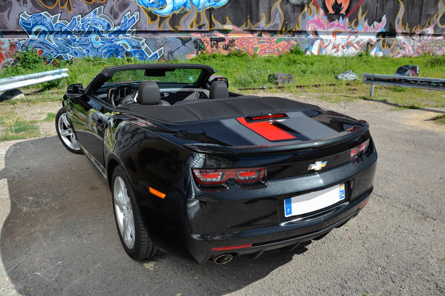 Rear view of a convertible with dual racing stripes and soft top cover.