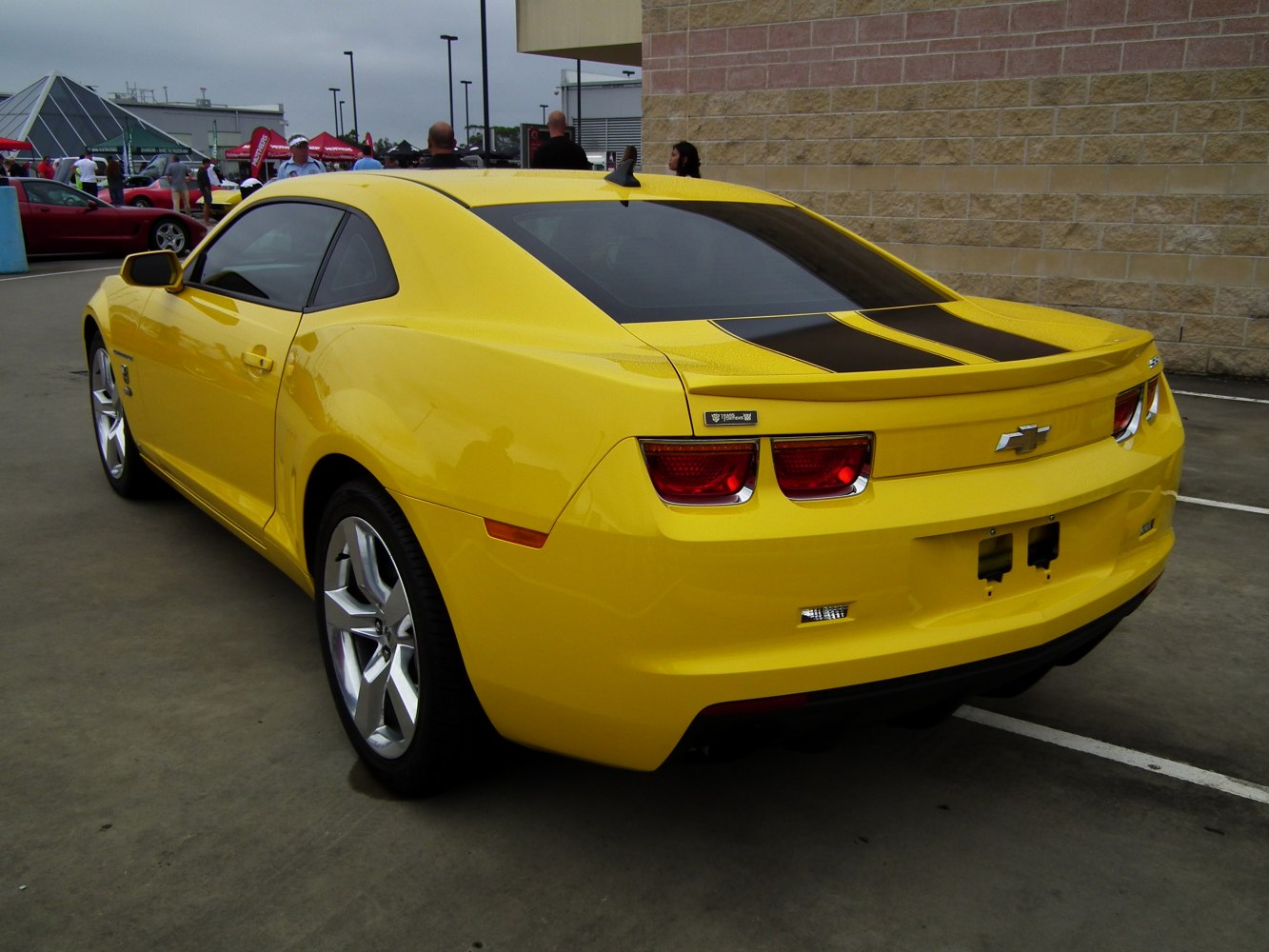 Yellow muscle coupe rear view with black racing stripes and alloy wheels.