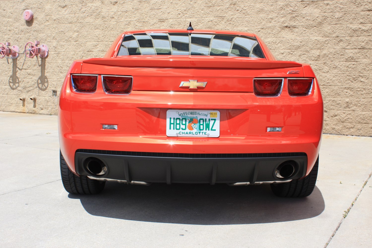 Rear view of a bright orange muscle sports car with dual exhaust and distinct taillights