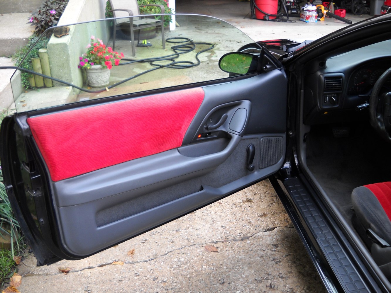 Interior car door panel with red upholstery and manual window crank.