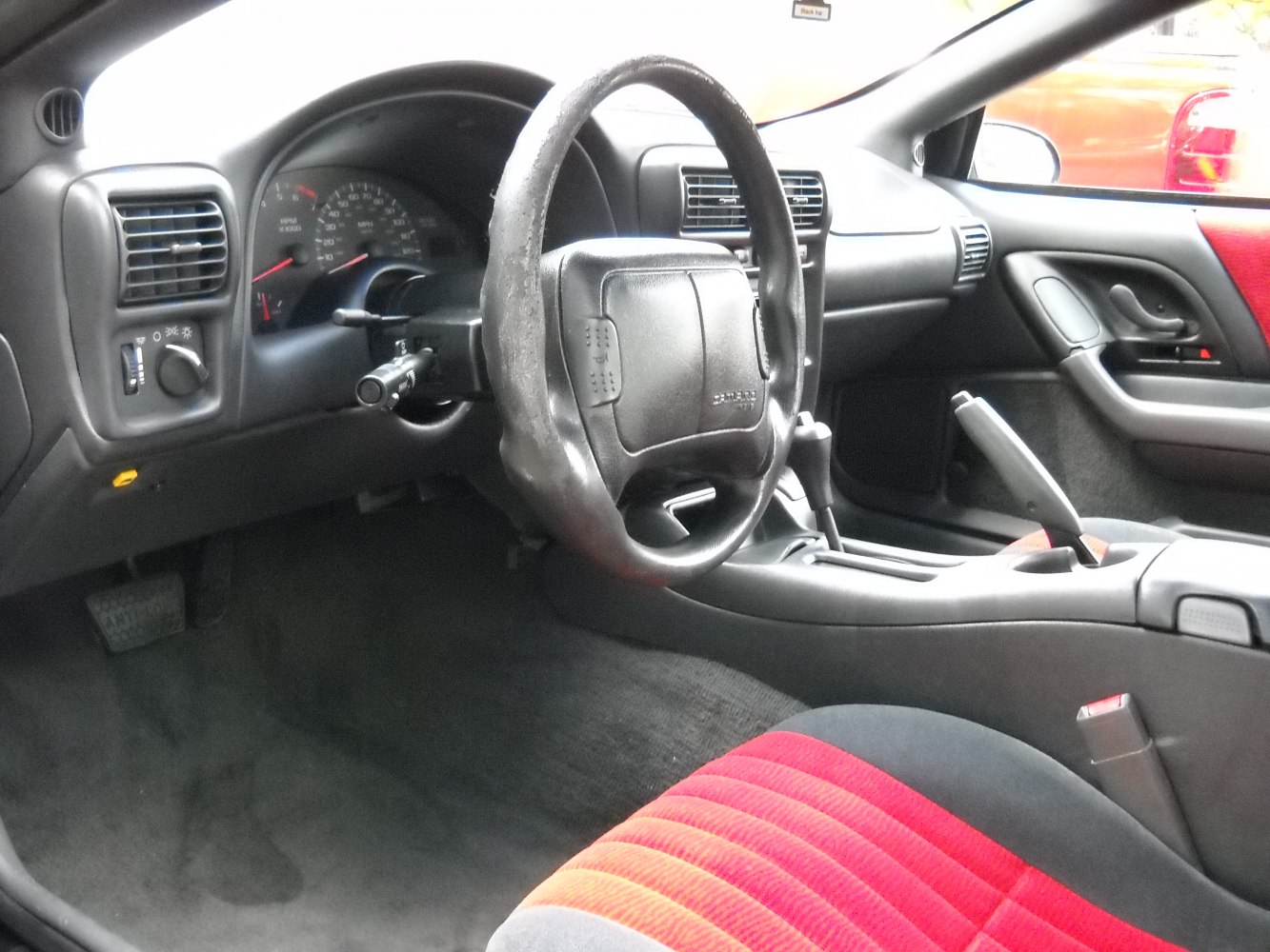 Steering wheel, dashboard, red-black seats, and gearshift inside a vehicle