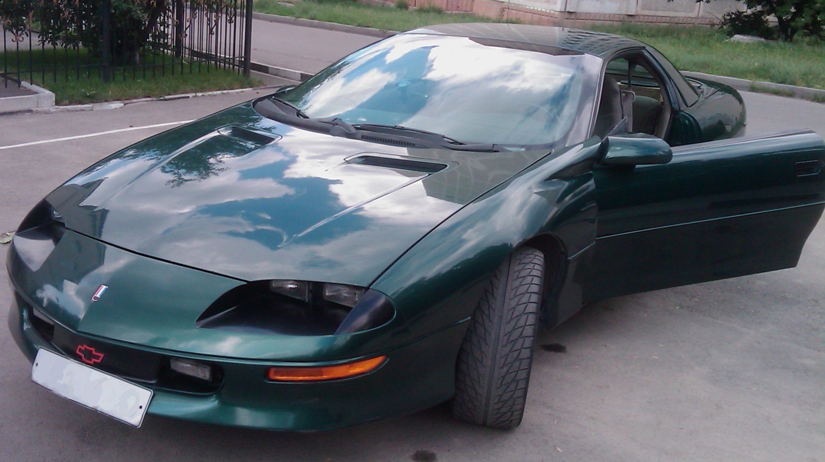 Front view of a sleek green vehicle with pop-up headlights and open driver's door