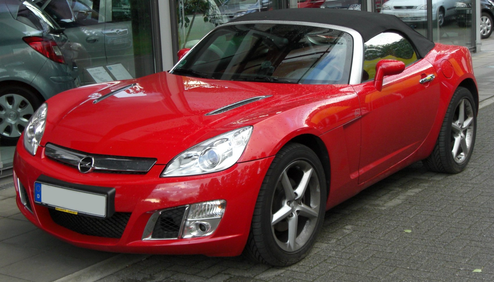 Red convertible sports car with sleek headlights and black soft top.