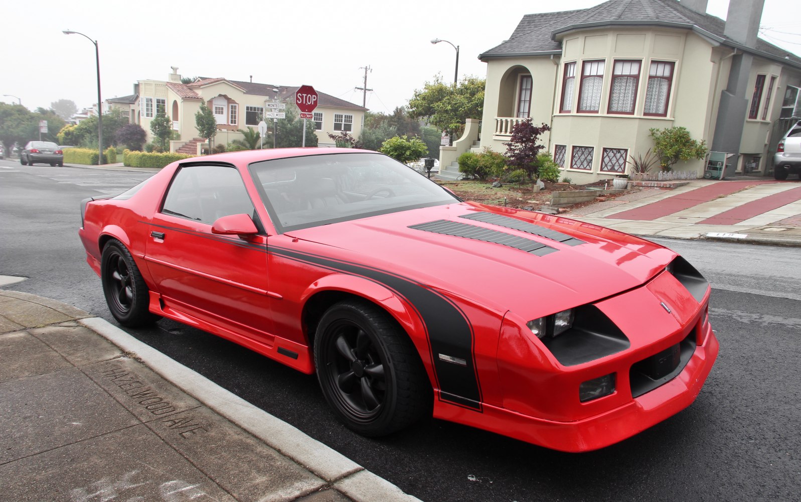 Red muscle car with black racing stripes, hood vents, and black wheels