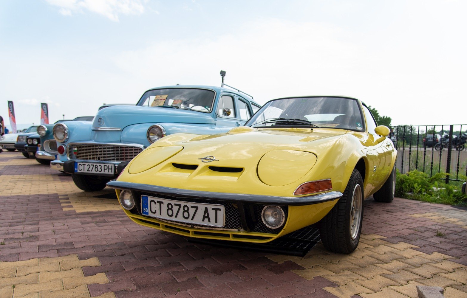 Pop-up headlights and dual hood vents on a vintage yellow sports coupe