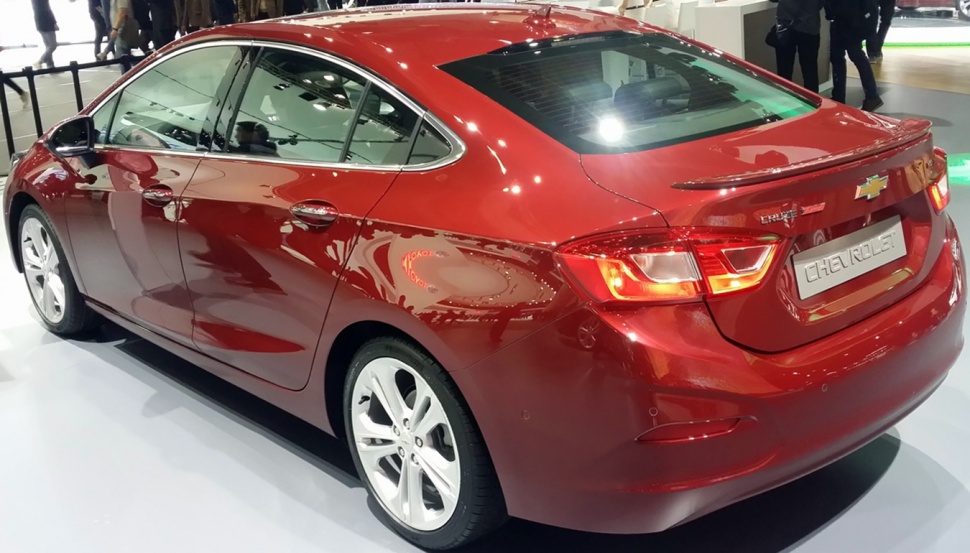 Rear-side view of a modern red sedan with illuminated taillights and alloy wheels.