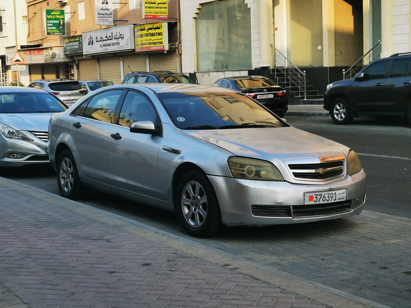 Silver sedan with front grille and fog lights parked on street curb.